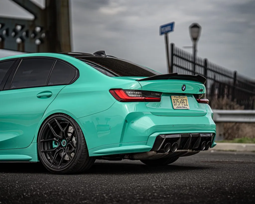 Teal BMW G80 M3 from behind with a carbon trunk spoiler and a finned carbon rear diffuser