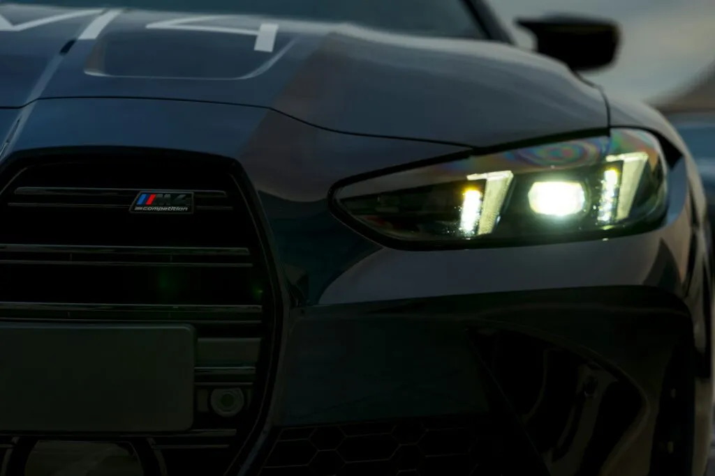 Close-up of a BMW M4 Competition grille with the M4 Competition badge on the top bar and a flat black radar panel covering the lowest bars of the driver's-side kidney